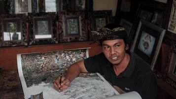 A person drawing on a large sheet of paper in a room with many framed pictures on the walls.