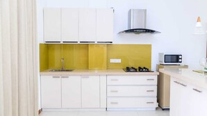 Een kleine keuken met witte kastjes, een gele achterwand, een magnetron en een gasfornuis.