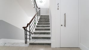 A staircase with marble steps and a wooden handrail, leading to a white door with a handle and a number plate.