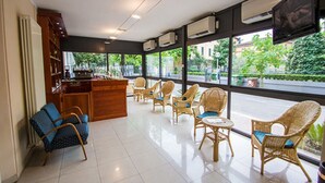 A hotel lobby with a reception desk, wicker chairs, and large windows offering a view of the street.