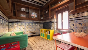 A room with a patterned tile floor, wooden walls, a green sofa, a yellow bookshelf, a red chair, and a table with a basket.