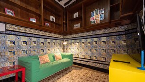 A room with a green sofa, a red table, and a yellow cabinet. The walls are decorated with patterned tiles.