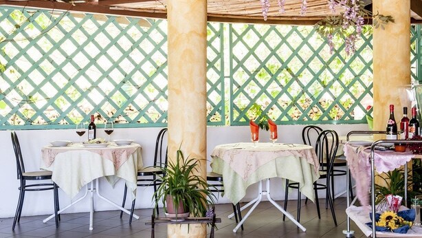 An outdoor patio with two tables, chairs, and a potted plant. - S'Ustiarvu (Orosei)