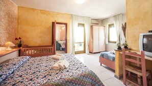 A bedroom with two beds, a desk, a TV, and a bathroom visible through an open door. - S'Ustiarvu (Orosei)