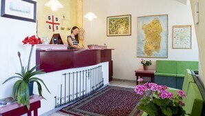 A reception area with a desk, a woman behind it, a map on the wall, and a green couch. - S'Ustiarvu (Orosei)