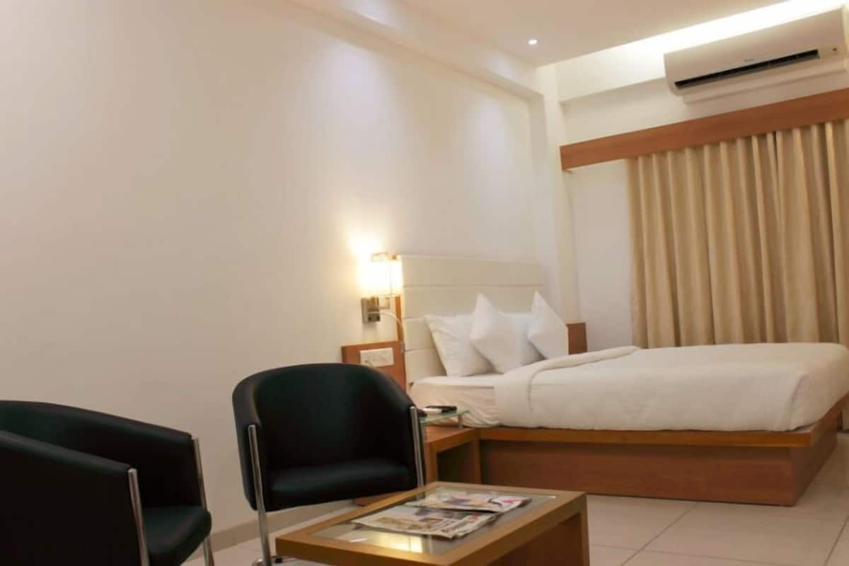 Quarto de hotel com uma cama, mesa de cabeceira, uma cadeira e uma mesa com uma revista.