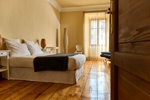 A bedroom with a wooden floor, a bed with white bedding, a bedside table, a lamp, and a chair. - B&B Al Cavour 34 (Trento)