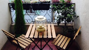 Un balcón pequeño con una mesa de madera y dos sillas, un farol y plantas en macetas.