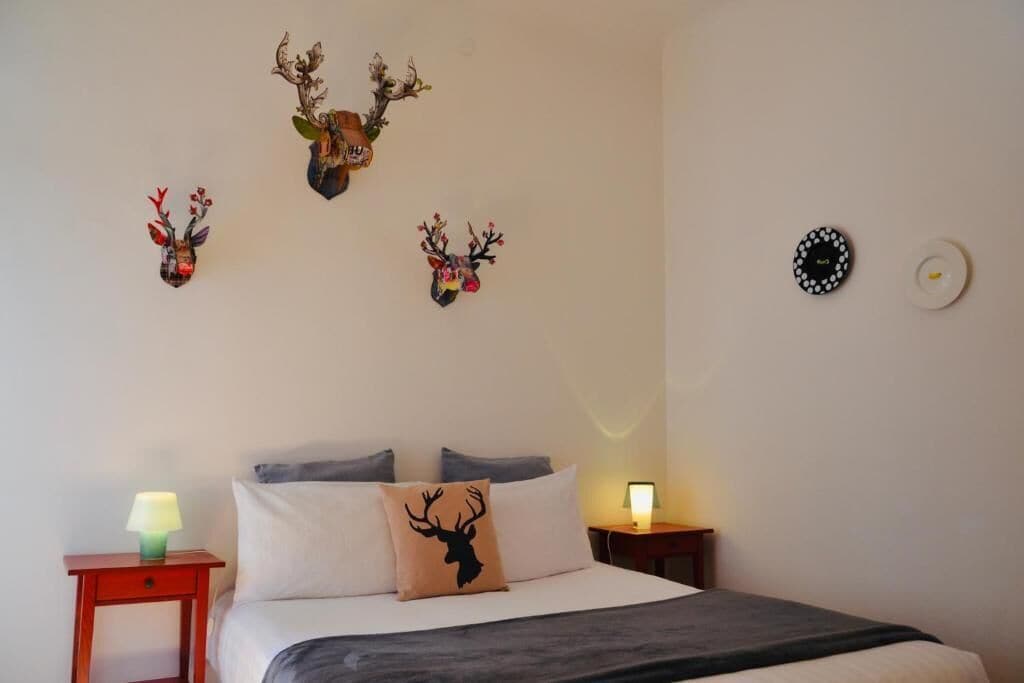 A bedroom with a bed, two bedside tables, and wall-mounted deer antlers.