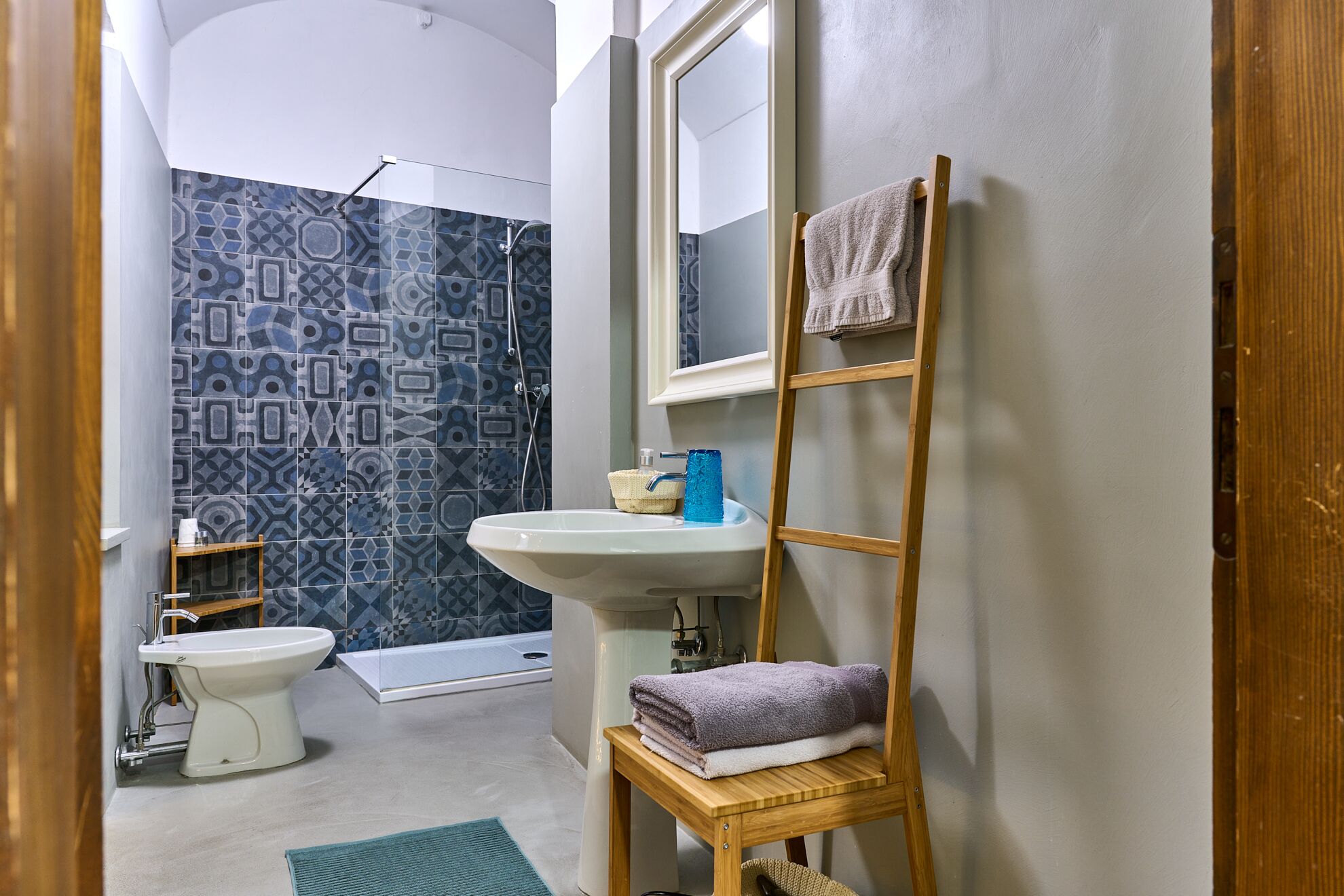 Une salle de bain équipée de toilettes, d’un lavabo et d’une douche. On y trouve un porte-serviettes avec des serviettes et une étagère en bois avec un panier.