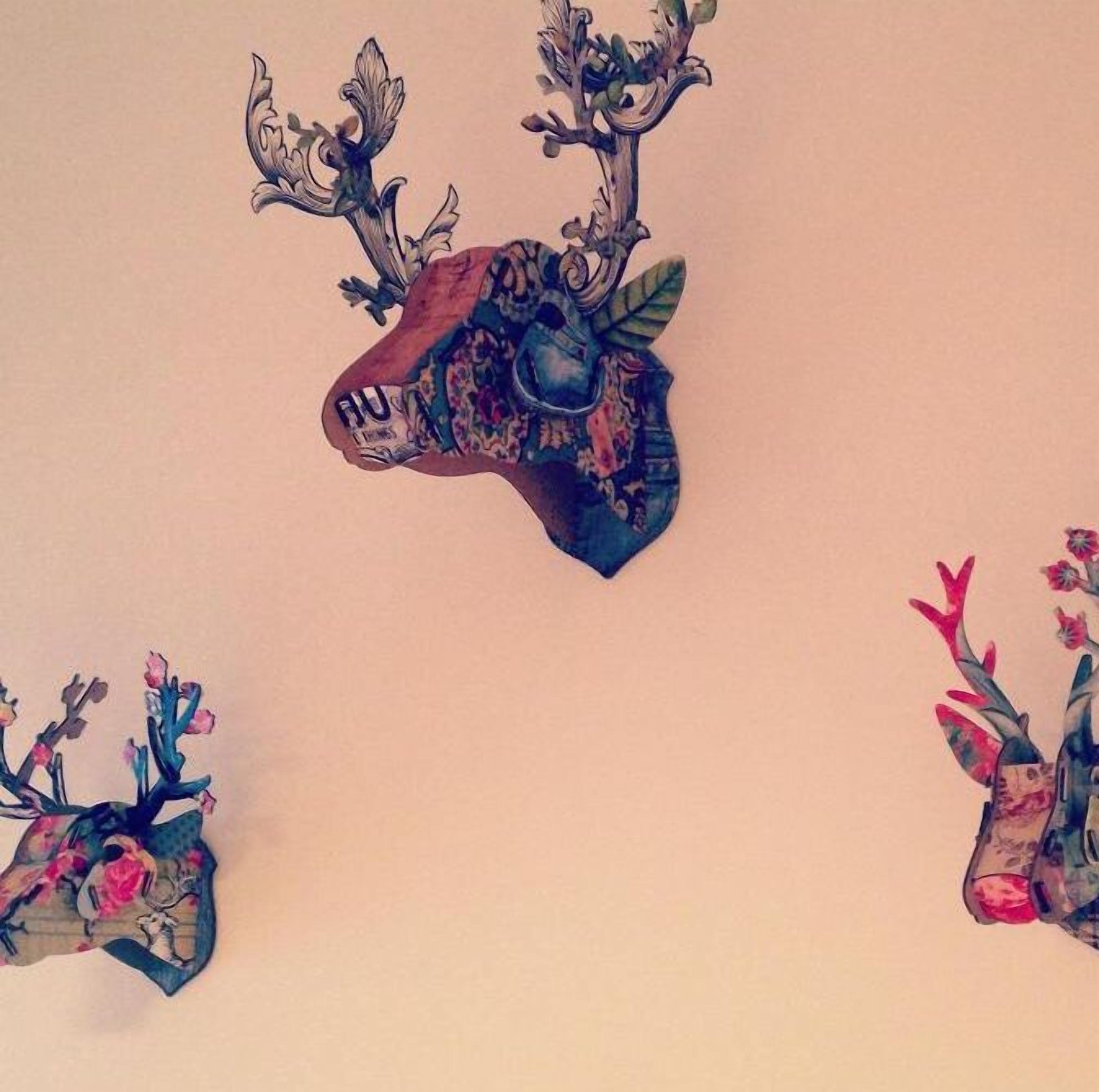 Een muur met drie gewelfde hertenkoppen, elk met unieke patronen en kleuren.
