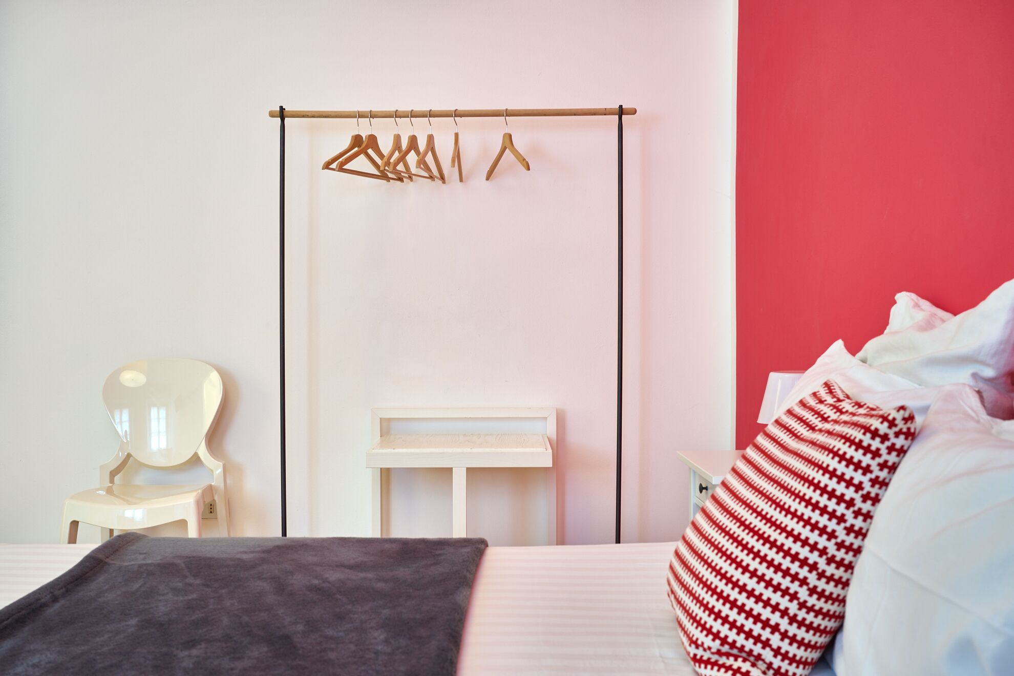 Un dormitorio con cama, mesita de noche, espejo, perchero de madera y una pared roja de acento.