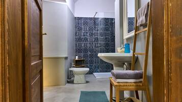 A bathroom with a toilet, sink, and shower. There is a wooden ladder and a towel rack.