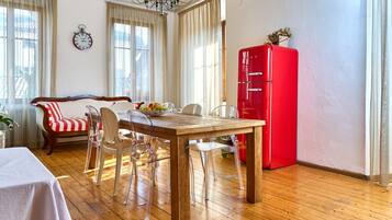 A dining area with a wooden table, clear chairs, a red refrigerator, and a sofa with striped cushions.
