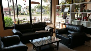 A living room with black leather sofas, a glass coffee table, and a white shelving unit with decorative items. - Suanluang Garden View Resort (Nong Khai)