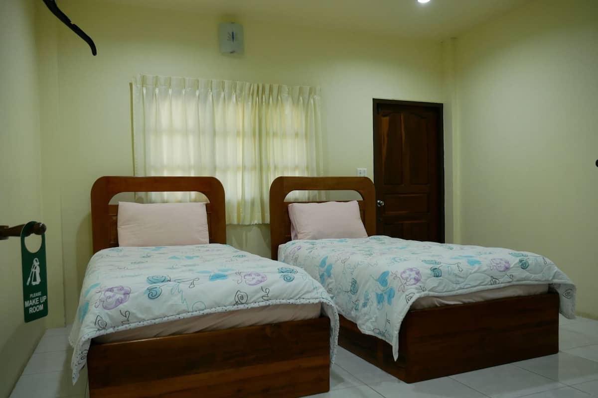 A room with two wooden beds, a door, a window with curtains, and a sign on the wall.