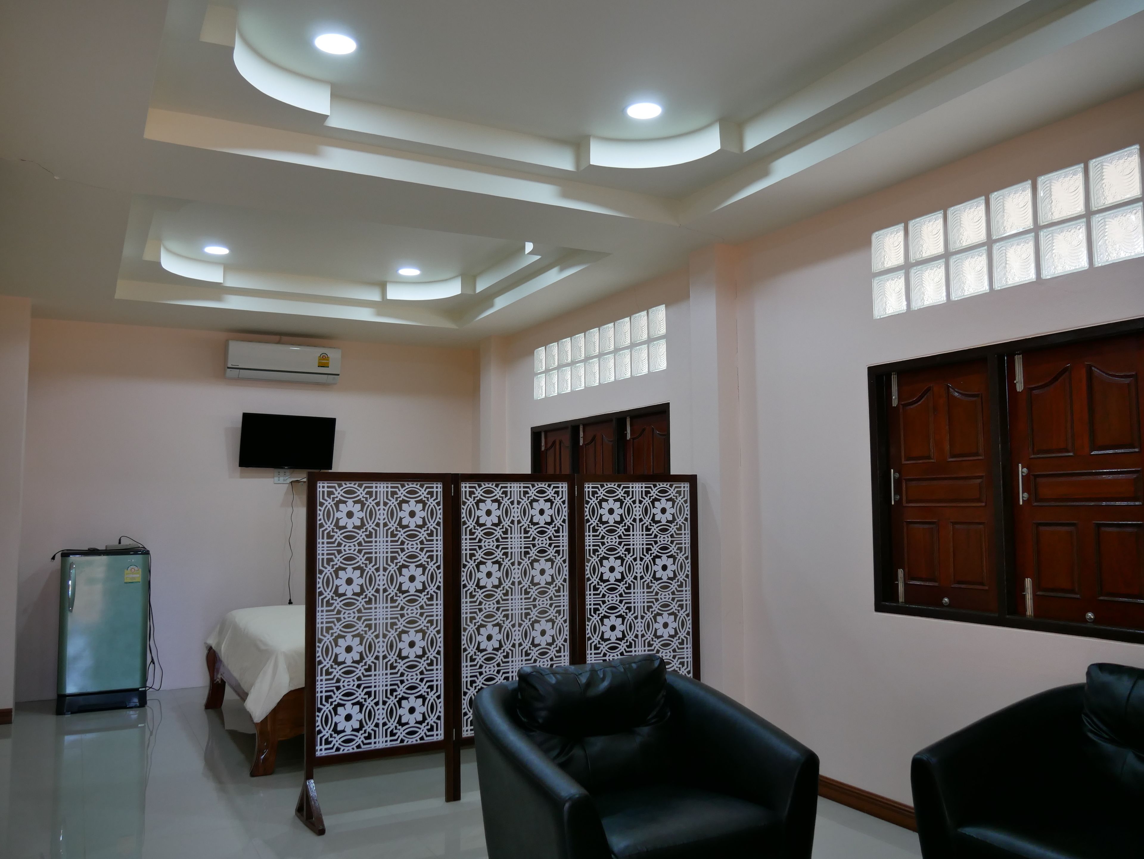 A room with a bed, a black leather chair, a refrigerator, a TV, and a decorative partition.