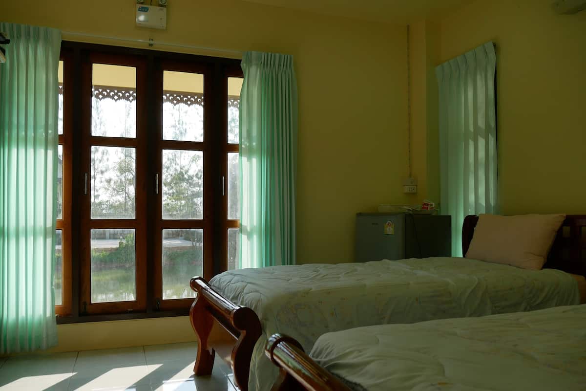 A room with two beds, a window with curtains, a small cabinet, and a ceiling fan.