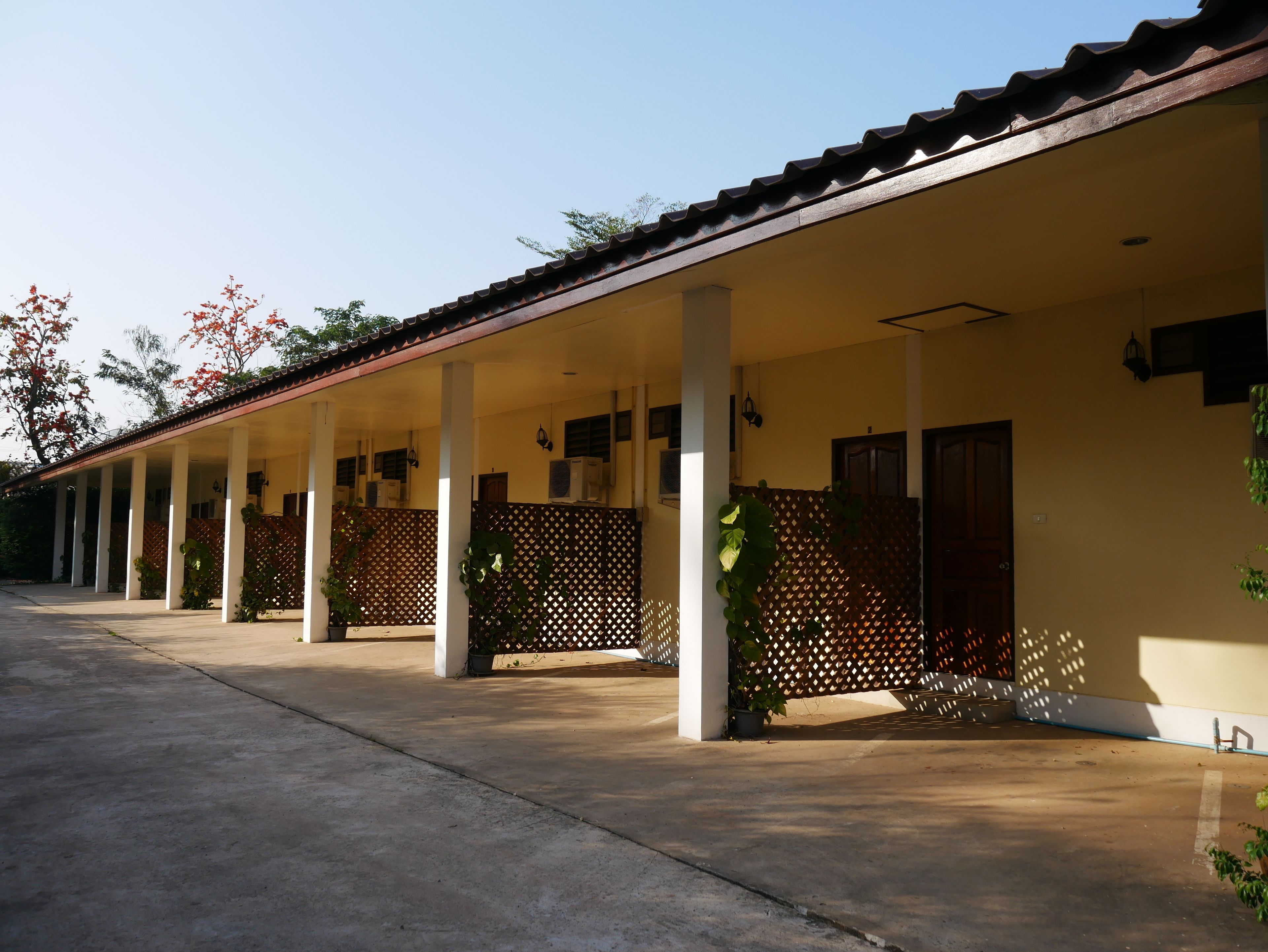 A covered outdoor area with columns, a tiled roof, and a fence with climbing plants.