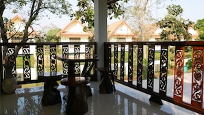 A covered outdoor area with a wooden table and chairs, a decorative fence, and a view of buildings in the background. - Suanluang Garden View Resort (Nong Khai)