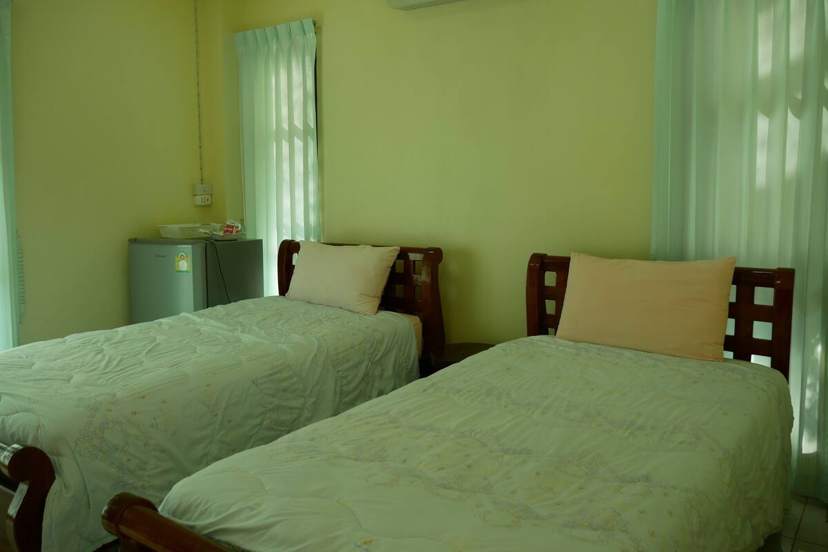 A room with two beds, a small desk, an air conditioner, and a window with curtains.