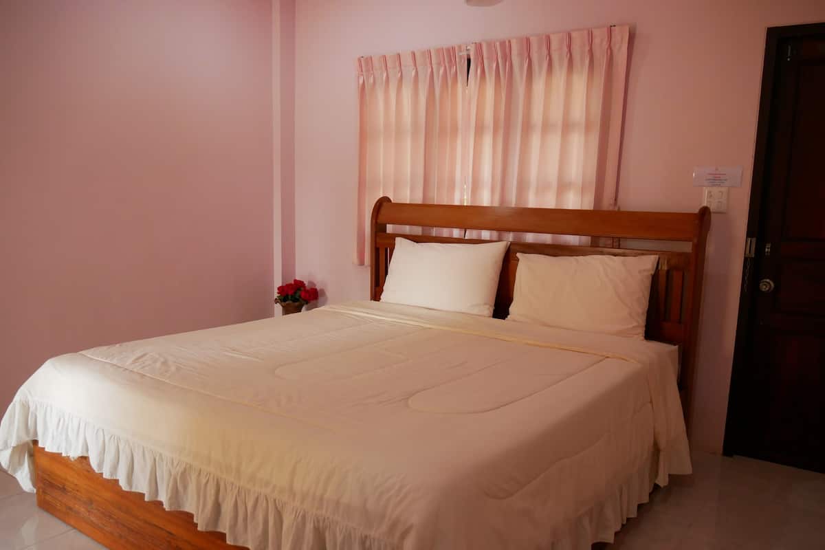 A neatly made bed with a wooden headboard, a vase with red flowers, and a door to the right.