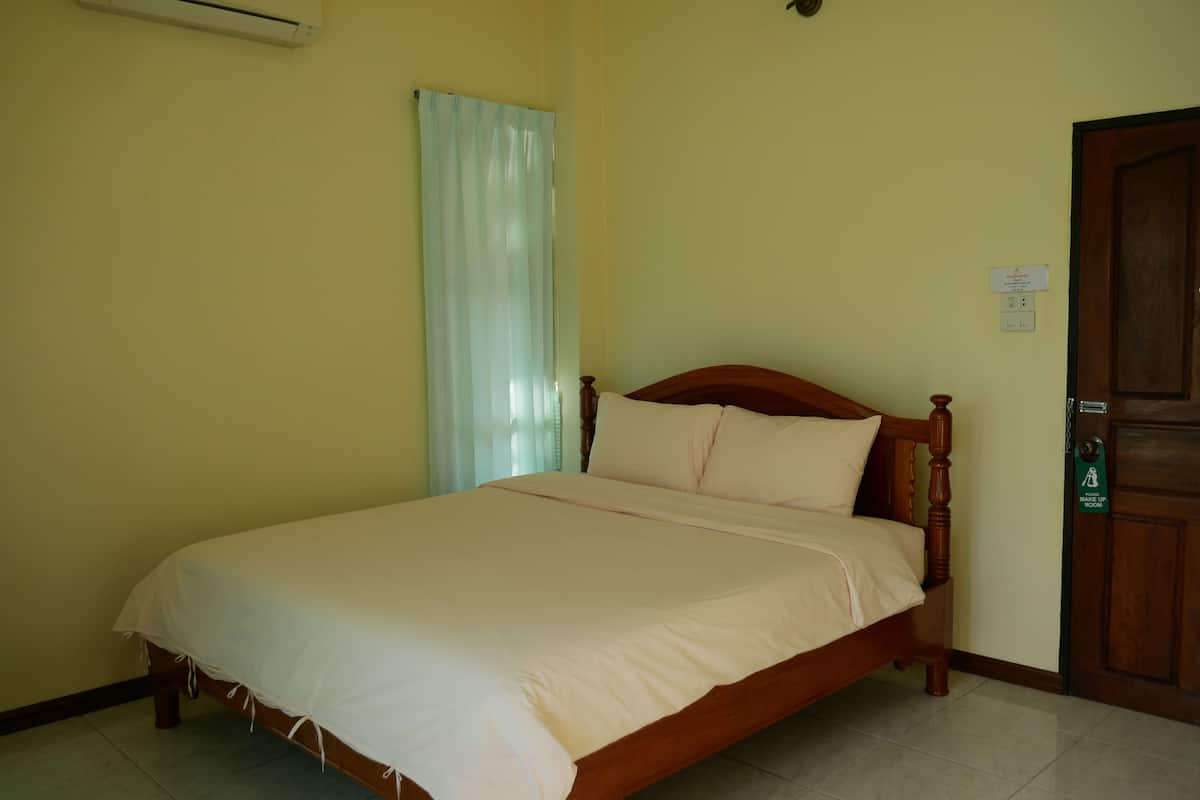A single bed in a room with a wooden headboard, a white bedspread, and a light blue curtain partially drawn.
