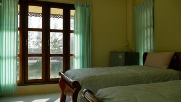 A room with two beds, a window with curtains, a small cabinet, and a wall-mounted air conditioner.