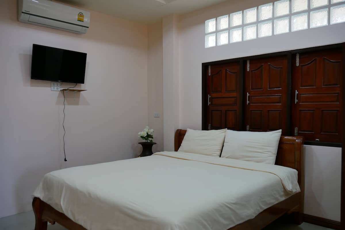 A bedroom with a bed, a TV mounted on the wall, and a window with decorative glass panes.