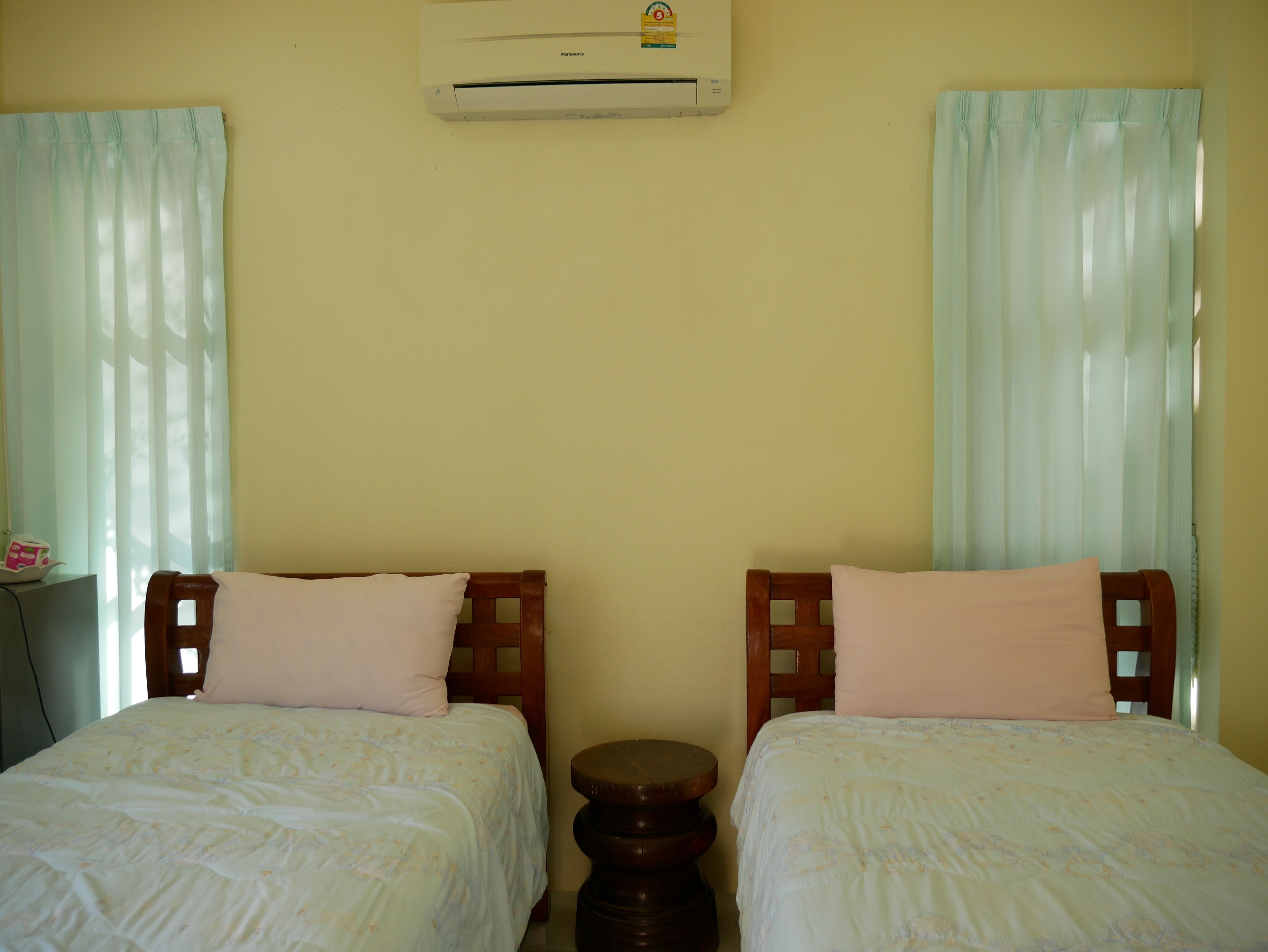 A room with two single beds, a wooden headboard, a small round table, and an air conditioning unit on the wall.