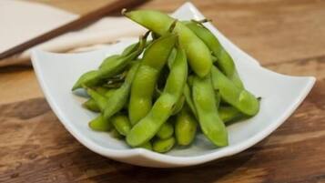 A white bowl filled with green edamame on a wooden surface.