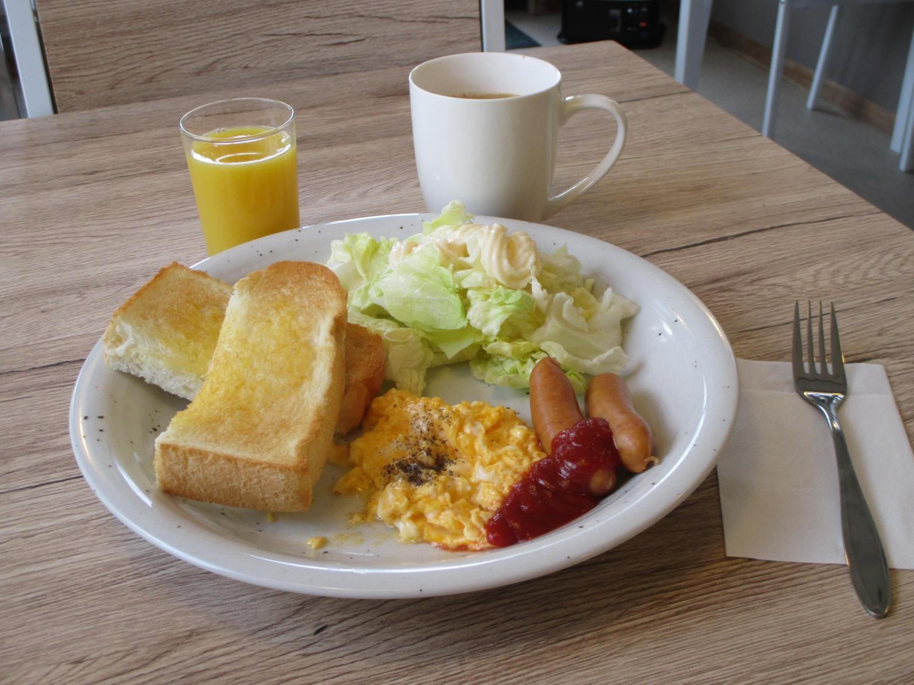 En frukosttallrik med rostat bröd, äggröra, ketchup och sallad på ett träbord.
