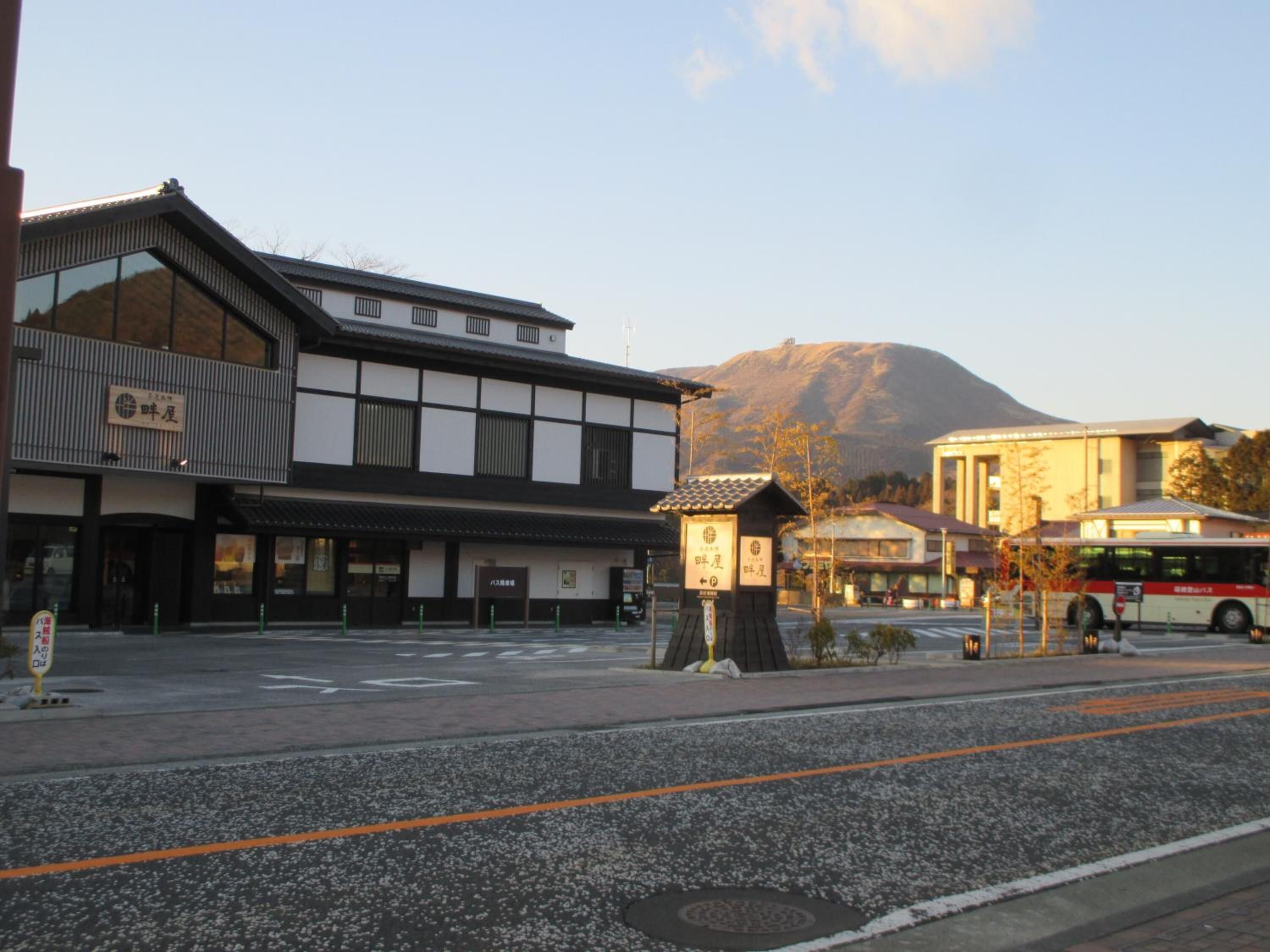 A traditional Japanese building with a modern facade, a bus stop, and a mountain in the background.