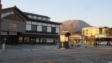 A traditional Japanese building with a modern facade, a bus stop, and a mountain in the background.