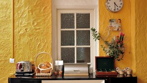 A room with a yellow textured wall, a window with frosted glass, a clock, a framed picture, and a small plant. - Hôtel Italia (Tours)