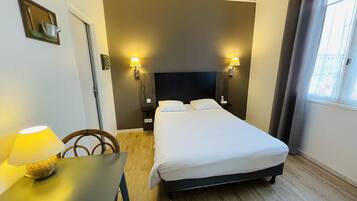 Una habitación de hotel con una cama, lámparas de noche, una mesa con lámpara, una silla y una ventana.