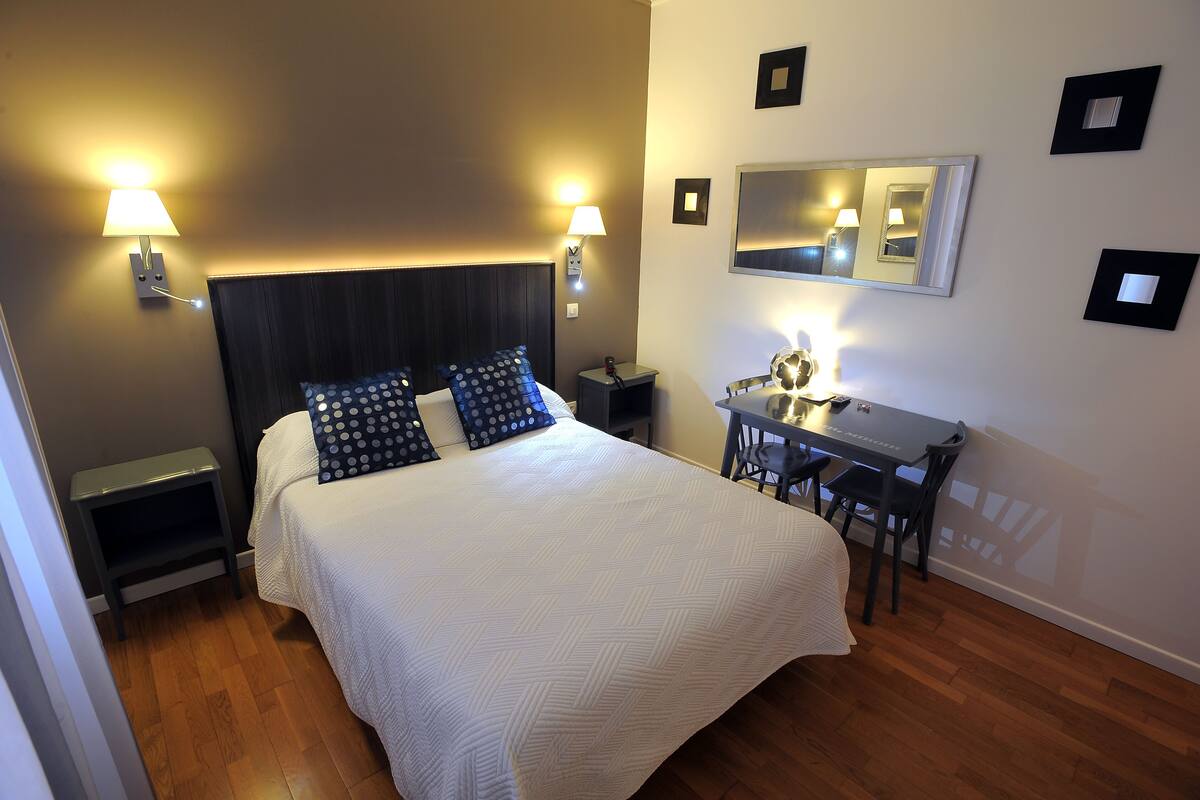 A hotel room with a bed, bedside lamps, a desk with a chair, and a mirror on the wall.