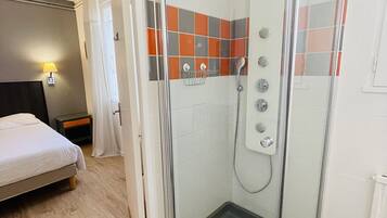 A hotel bathroom with a glass-enclosed shower, a bed, and a nightstand.