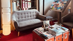 A cozy room with a grey sofa, a red suitcase, and a bookshelf filled with books. - Hôtel Italia (Tours)