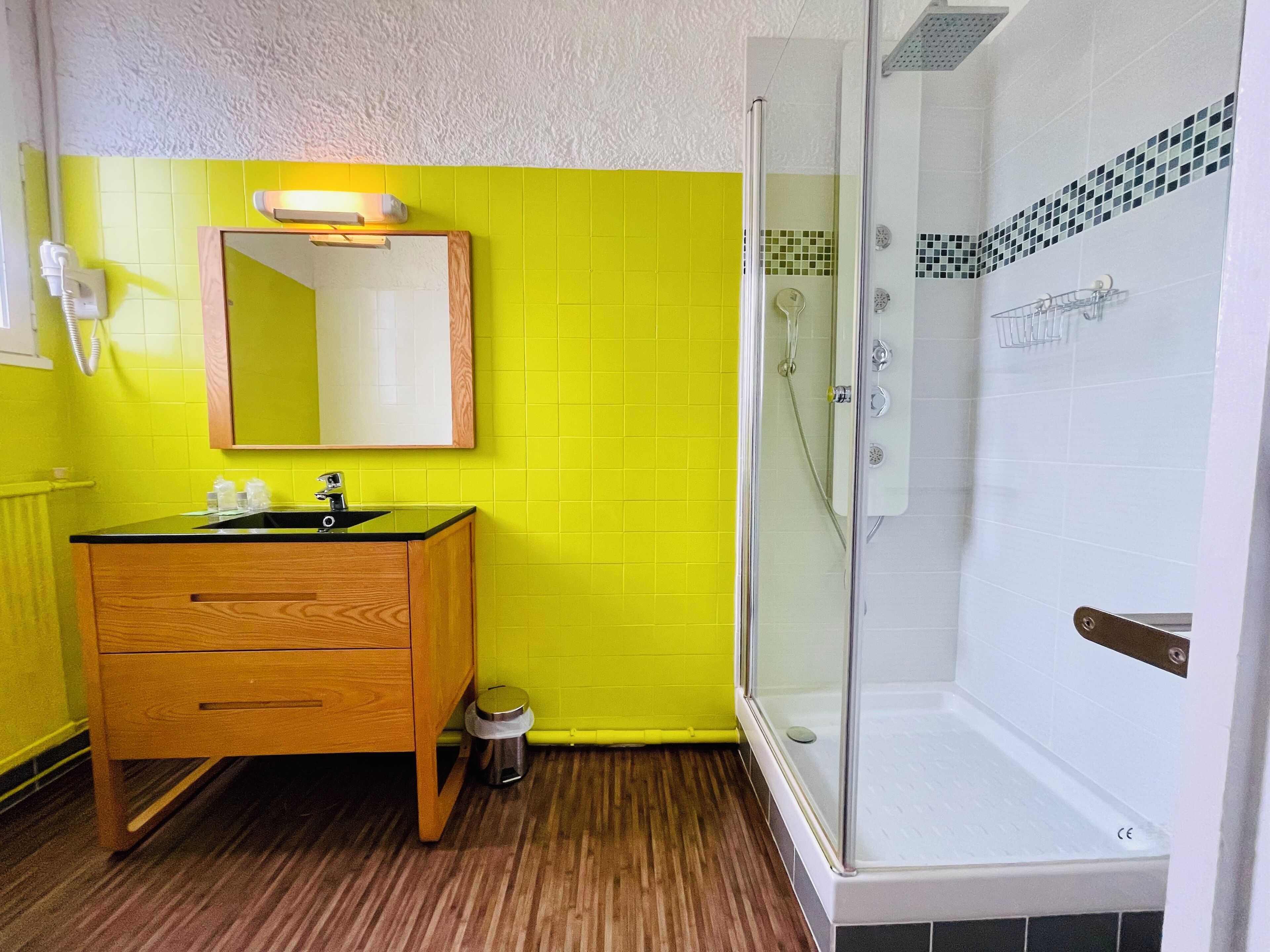 Un baño con tocador de madera, espejo, lavamanos y cabina de ducha con mampara de vidrio.