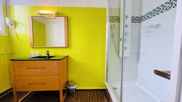 Un baño con tocador de madera, espejo, lavamanos y cabina de ducha con mampara de vidrio.