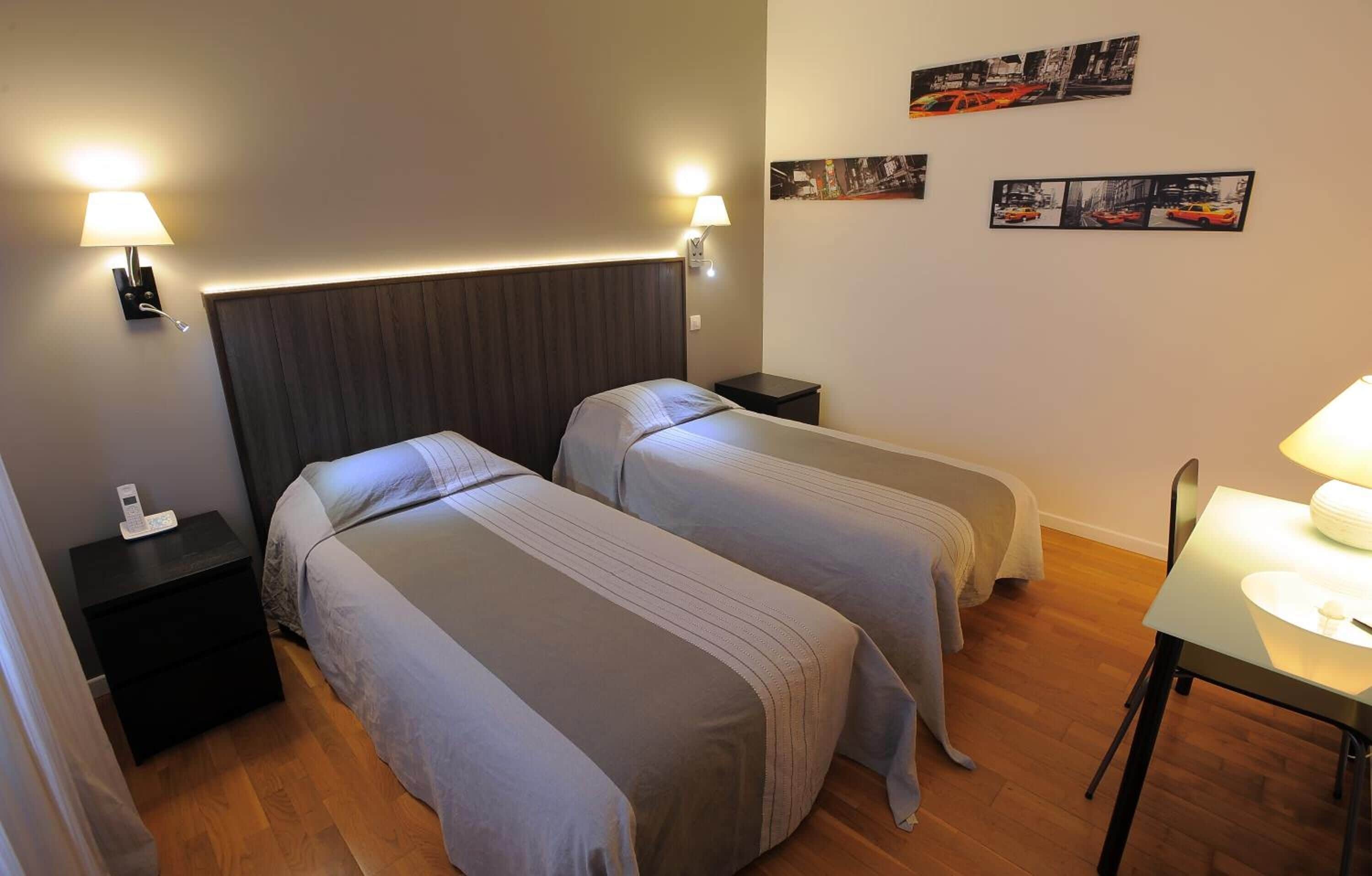Habitación de hotel con dos camas individuales, una mesita con lámpara, una mesita de noche con teléfono y decoración en la pared.