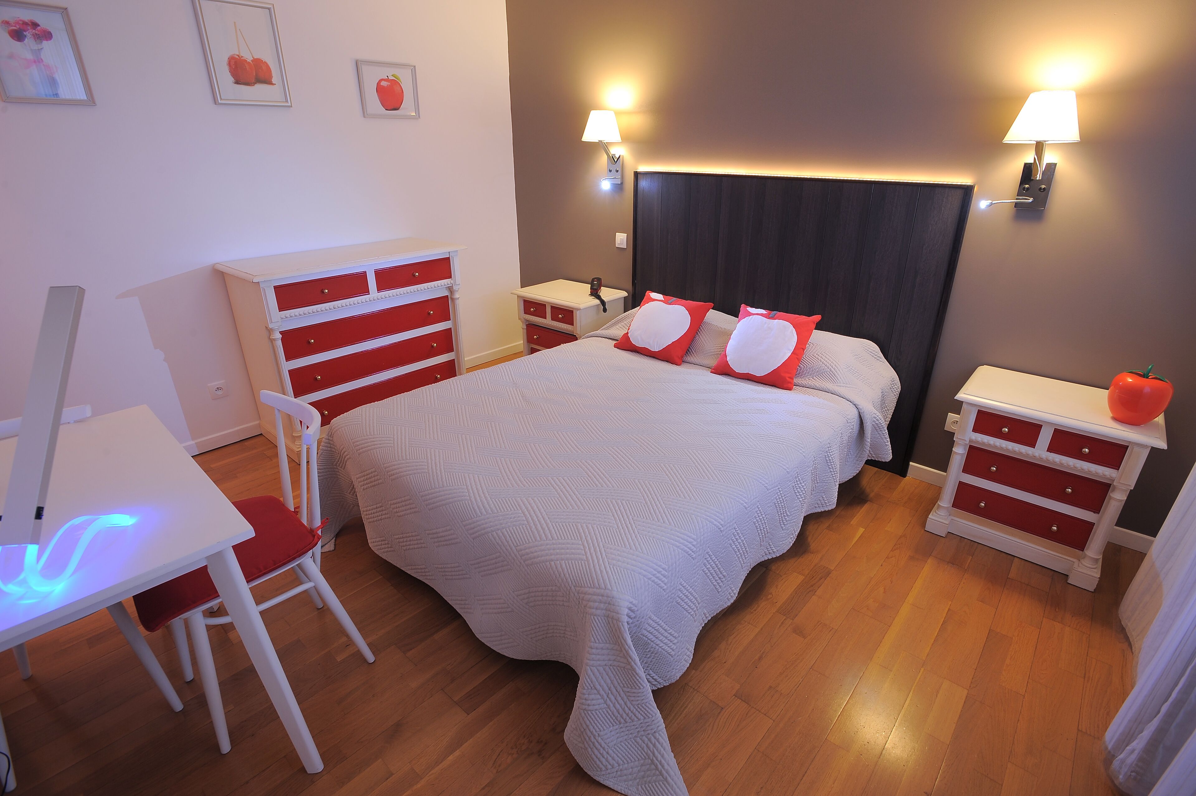 A neatly arranged bedroom with a bed, bedside tables, a desk, and a chair.