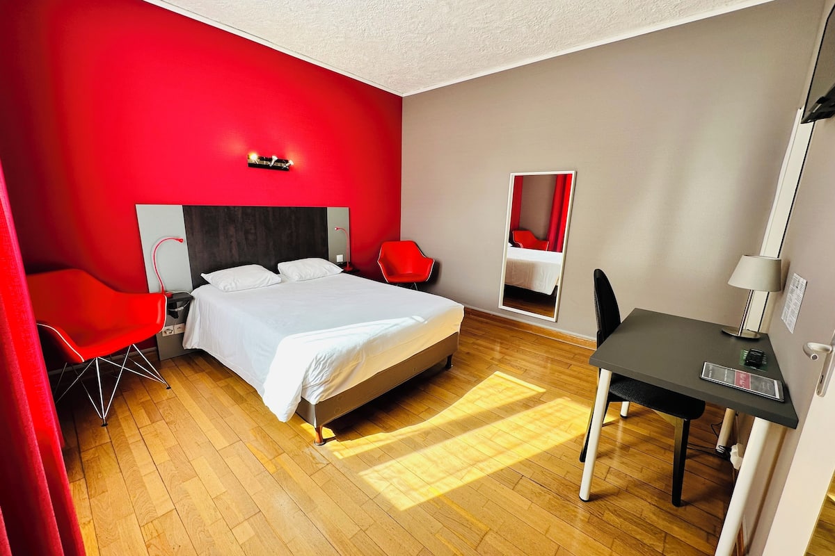 A hotel room with a bed, a desk, a chair, and a mirror.