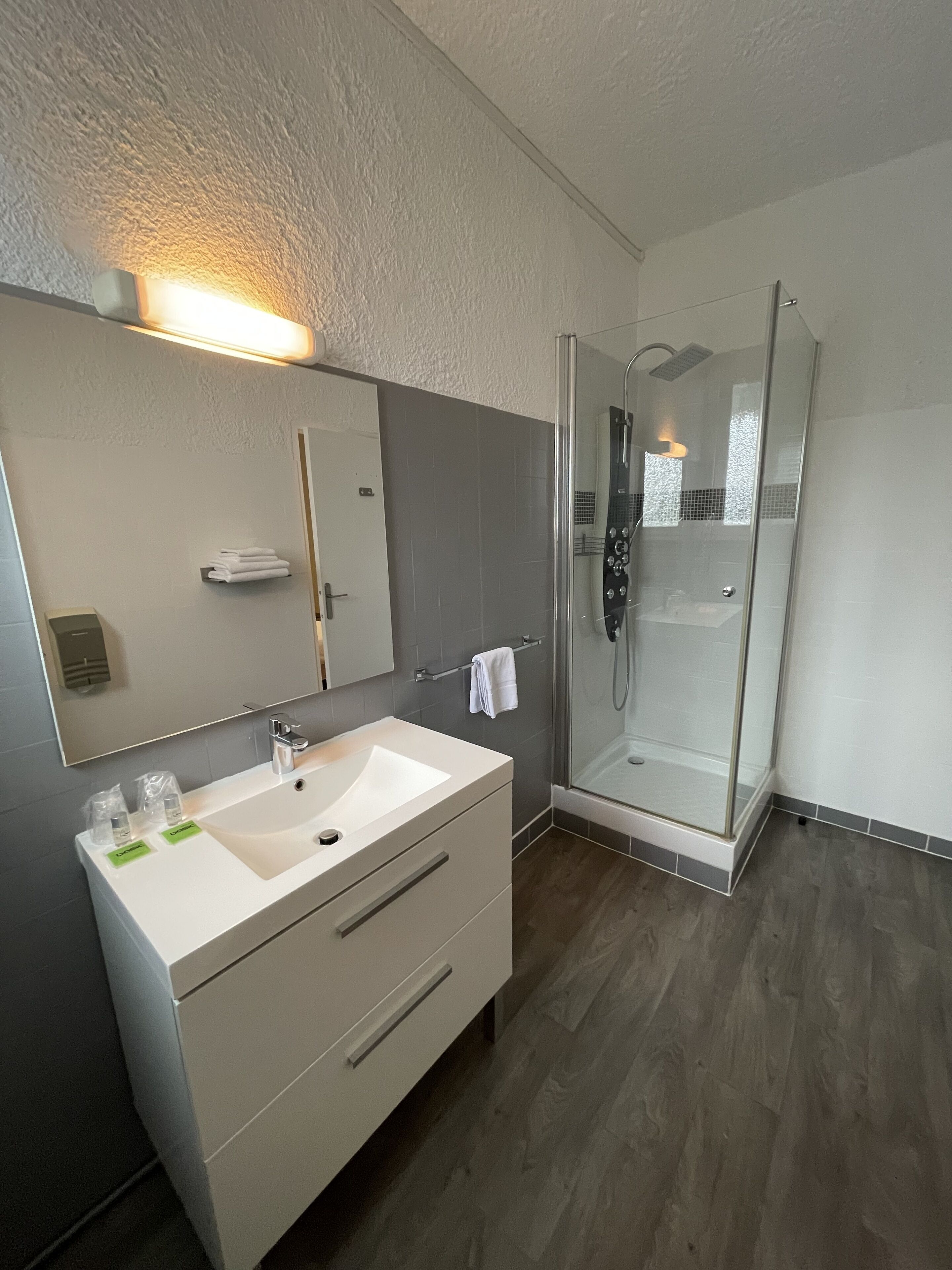 Un baño moderno con un tocador blanco, una cabina de ducha de vidrio y un espejo grande sobre el lavamanos.