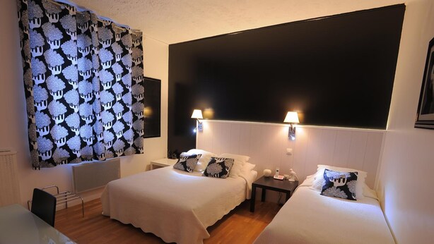 A hotel room with two beds, a desk, and a large window with a patterned curtain. - Hôtel Italia (Tours)