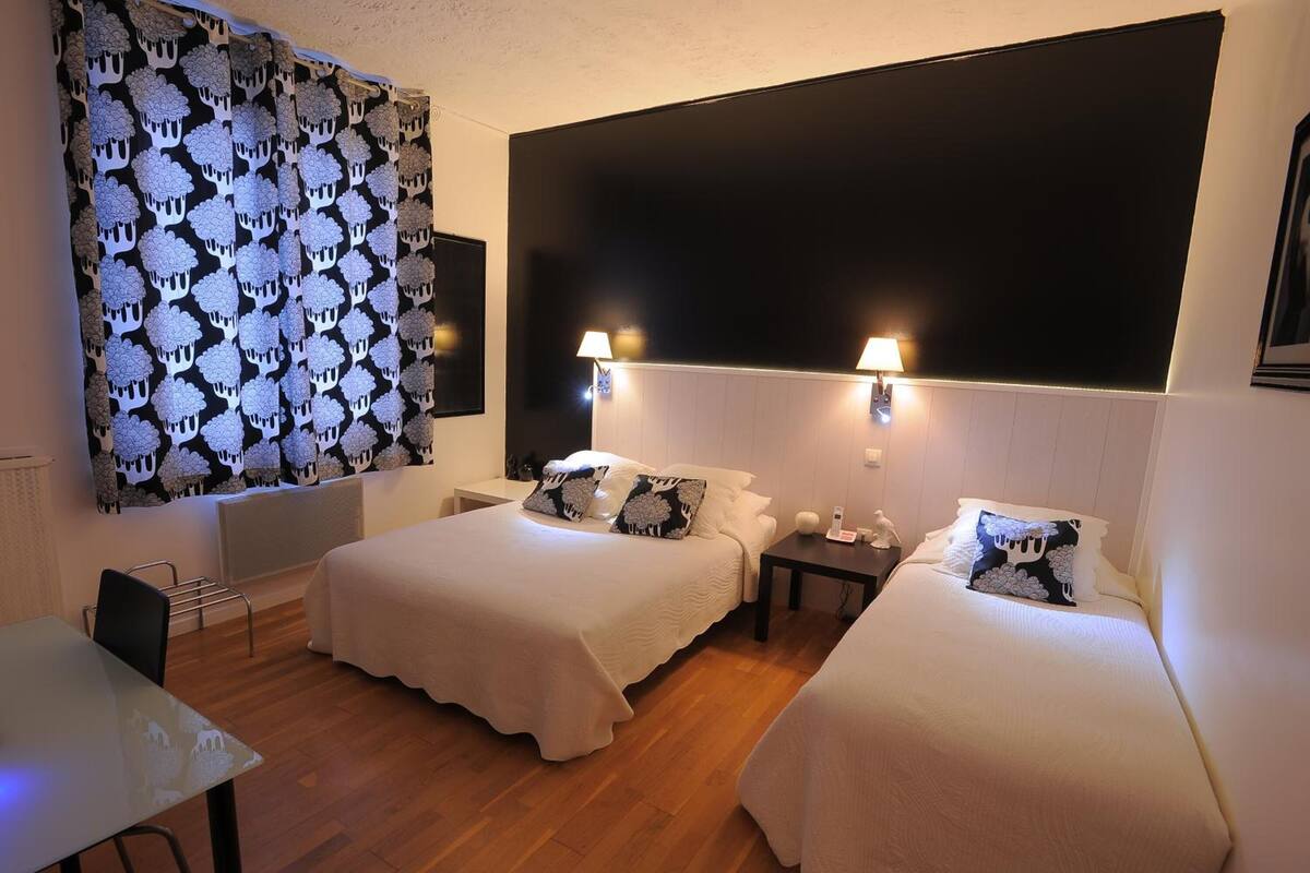 A hotel room with two beds, a desk, and a large window with a patterned curtain.