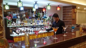 Zona de bar amb varietat de botelles i gots exposats a prestatgeries, barra amb un disseny decoratiu i llums penjants.