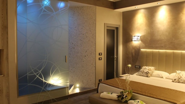 A modern bedroom with a large bed, a nightstand, a wall-mounted lamp, and a sliding glass door with a decorative pattern.
