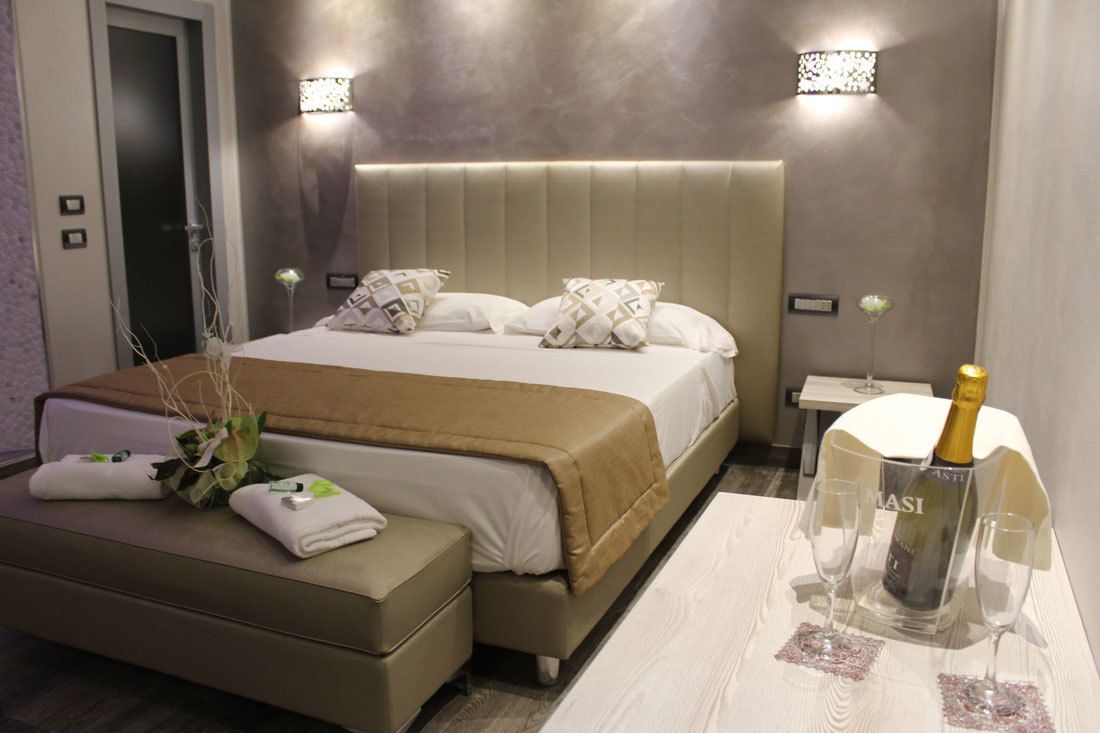 Une chambre d’hôtel moderne avec un grand lit, une table de chevet sur laquelle se trouve une bouteille de champagne, et une petite table avec deux verres.